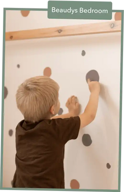 Child in a dark shirt drawing or marking on a white wall with dots.